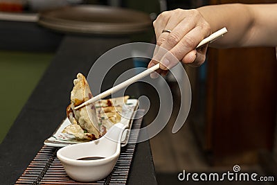 Woman's hand with chopsticks dipping a gyoza in soy sauce and then gobbling it up with delight Stock Photo