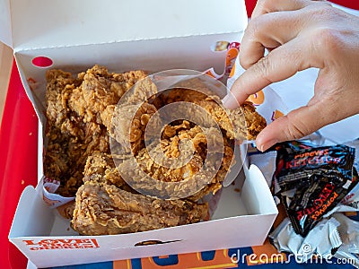 Woman`s hand grabbing piece of Popeyes Louisiana Chicken from dinner box in restaurant Editorial Stock Photo