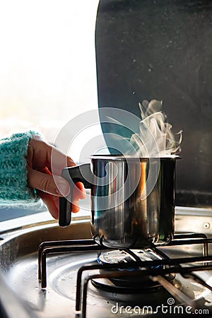 woman's hand grabbing a saucepan with boiling drink in a camper van. camping in winter Stock Photo