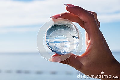 Woman hand holding a crystal ball, looking through to the ocean and sky. Creative photography Stock Photo