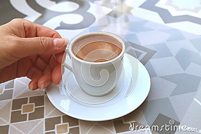 Woman`s Hand Holding a Cup of Turkish Coffee Served on a Moorish Pattern Table Stock Photo