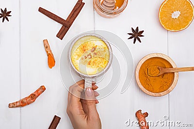 Woman`s hand holding a cup with turmeric latt or golden milk on white table Stock Photo