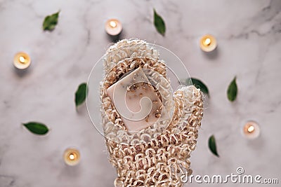 Woman's hand holding diy oats soap. Knitted sisal washcloth in mitten shape. Burning candles and marble background Stock Photo
