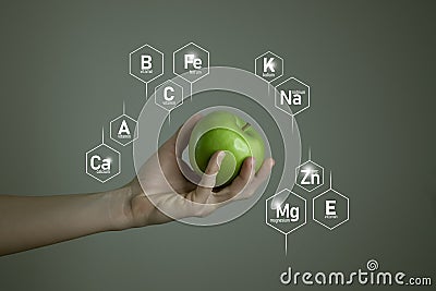 Woman`s hand holding green apple, microelement icons in molecular hexagons on grey background. Stock Photo