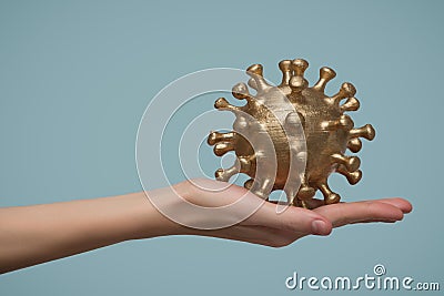 Woman`s hand holds a gold-colored virus model. Blue background Stock Photo