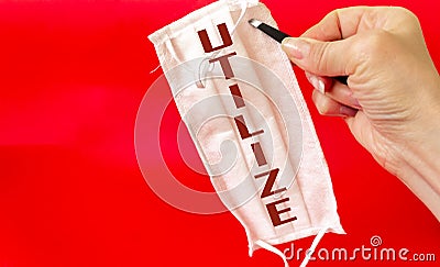 A woman`s hand holds a medical mask with the text Utilize, on a red background. Stock Photo