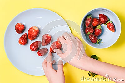 Woman`s hand holds a strawberry. Blue plate with summer berries. Flat lay, top view Stock Photo