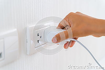 Woman`s Hand Inserting Electrical Power Cord Plug into Receptacle on wall outlet Stock Photo