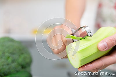 Woman`s hand peeling green fresh zucchini. Woman preparing delicious and healthy food in the home kitchen. Healthy diet concept Stock Photo