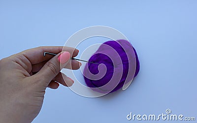 Woman`s hand with pink manicure holding the steel needle above piece of violet wool on white background. Concept of felting creati Stock Photo