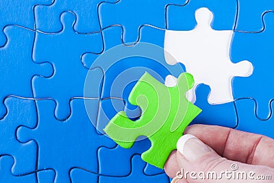 Woman's hand placing missing piece in Jigsaw puzzle signifying Stock Photo