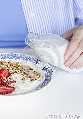 Woman`s hand pouring plant based milk into homemade granola with fresh organic strawberries and yogurt in the vintage plate. Stock Photo