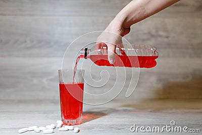 A woman's hand pours a red sports drink or lemonade into a glass Cup from a plastic bottle. Energy drink in glass and plastic bot Stock Photo