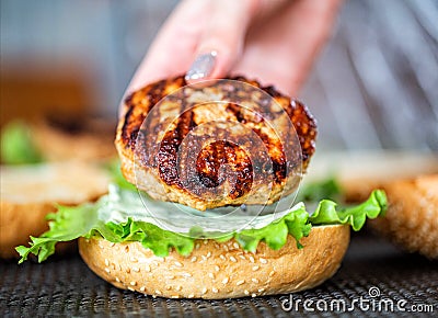 A woman& x27;s hand puts a juicy beef cutlet on a burger bun. Making burgers at home, close-up Stock Photo