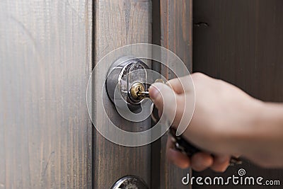 Woman`s hand puts the key in the keyhole of wooden door. Home se Stock Photo