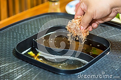 A woman`s hand is putting dried oysters in broth in an electric stove to make Japanese broth Stock Photo