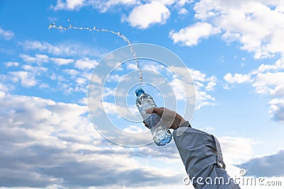 A woman`s hand raises a highly transparent bottle of pure mineral water. Splashes are flying against the background of a blue sky Stock Photo