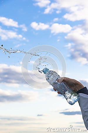 A woman`s hand raises a highly transparent bottle of pure mineral water. Splashes are flying against the background of a blue sky Stock Photo