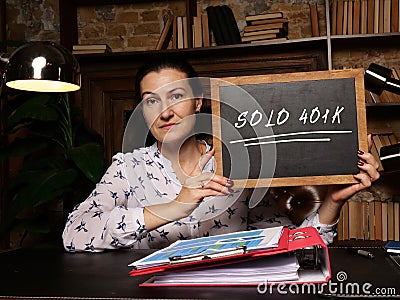 Woman`s hand showing chalkboard with phrase SOLO 401K - closeup shot on grey background Stock Photo