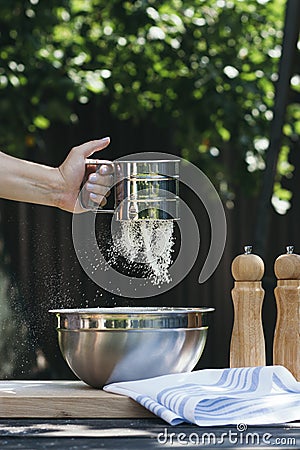 A woman`s hand sifting flour for baking Stock Photo