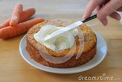 Woman`s hand spreads frosting on a baked carrot cake, wooden table Stock Photo