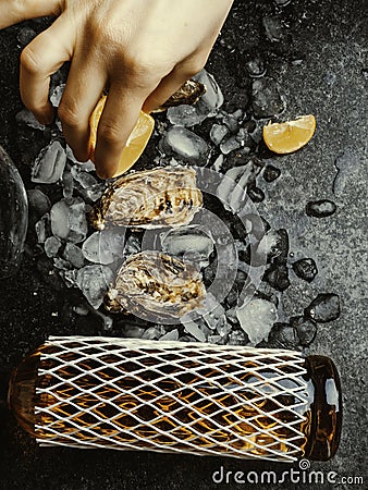 Woman's hand squeezes juice from lemon on oyster shell, dark stone background. Wine bottle and glass. Food aphrodisiac Stock Photo
