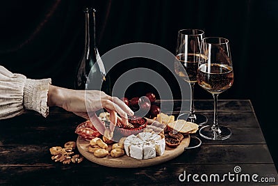 Woman`s hand takes crackers from the Appetizers board with assorted cheese, meat, sausage rosette, grape and cookies Stock Photo