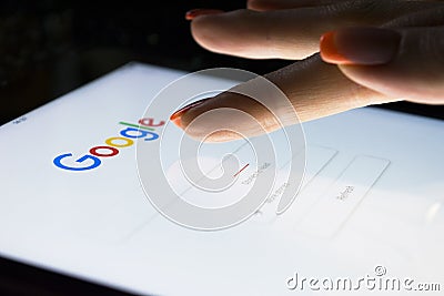 A woman`s hand is touching screen on tablet computer iPad Pro at night for searching on Google search engine. Google is the most Editorial Stock Photo