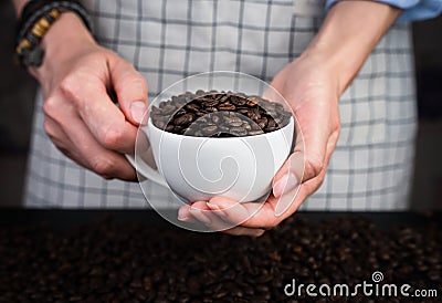 Woman`s hands hold a white cup with fresh fragrant coffee beans. Natural coffee. Close-up. Selective focus Stock Photo