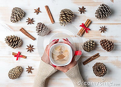 Woman`s hands holding mug of coffee with cinnamon, star anise and pine cones over white wooden table. Stock Photo