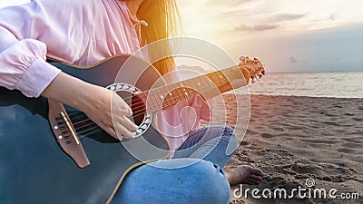 Woman`s hands playing acoustic guitar, capture chords by finger on sandy beach at sunset time. playing music concept Stock Photo