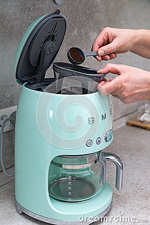 Woman`s hands are pouring ground coffee into a SMEG brand coffee maker on the kitchen table Editorial Stock Photo