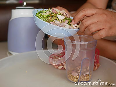 A woman`s hands preparing / putting food ingredients in a small blender cup for blending for cooking food at home Stock Photo