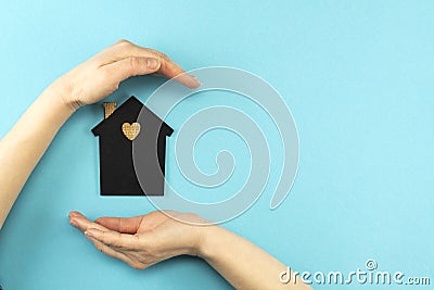 Woman`s hands surround a mock-up of a dark house on a blue background. Family, real estate and insurance concept, flat lay, top Stock Photo