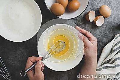 Woman& x27;s hands whisk eggs in bow. Cooking omlette for breakfast. Top view, flat lay of cooking process. Dark background Stock Photo