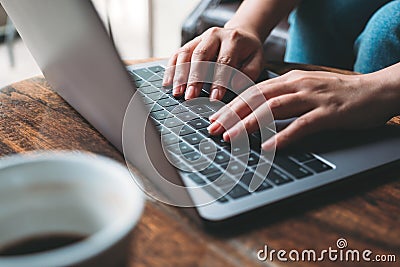 A woman`s hands working and typing on laptop keyboard with coffee cup on wooden table Stock Photo