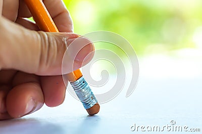 Woman left Hand hold orange triangular pencil, Rubber to delete from white paper, Bokeh green garden background, Notebook, Close Stock Photo