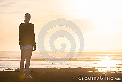 Woman on sandy beach watching sunset. Stock Photo