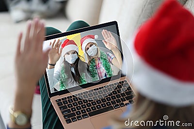 Woman in santa claus hat holds laptop on knees and communicates with her friends in protective masks on face portrait Stock Photo