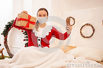 Woman in santa claus Jacket holds Phone and communicates with her friends in protective masks on face. Remote celebration of new Stock Photo
