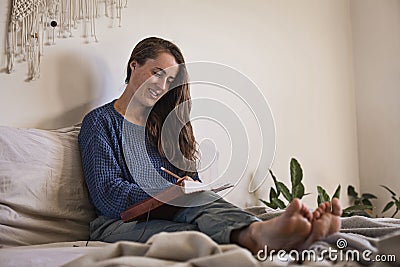 Woman sat writing her diary in bed Stock Photo