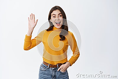 Woman saying hello and smiling friendly. Cheerful girl say goodbye or greet you, waving raised hand and looking at Stock Photo