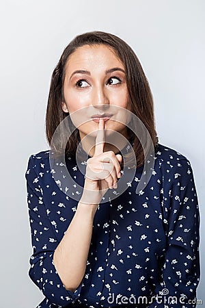 Woman saying hush be quiet with finger on lips gesture isolated on gray wall background. Portrait of emotional girl, saying `shh Stock Photo