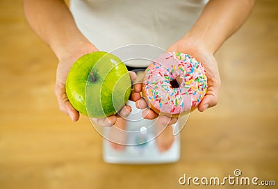 Woman on scale measuring weight holding apple and donuts choosing between healthy or unhealthy food Stock Photo