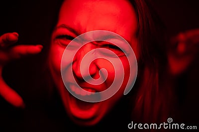 Woman screaming close-up to camera in red neon light, furious face, hysterics Stock Photo