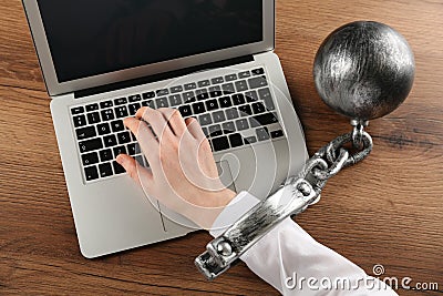 Woman shackled with ball and chain typing on laptop at wooden table, above view. Internet addiction Stock Photo