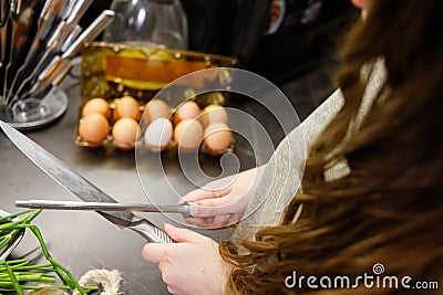 Woman sharpening kitchen knife with grindstone in the kitchen, kitchen knife. Close up view on hands Stock Photo