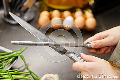 Woman sharpening kitchen knife with grindstone in the kitchen, kitchen knife. Close up view on hands Stock Photo