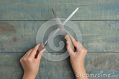 Woman sharpening knife at light blue wooden table, top view Stock Photo