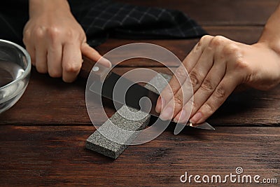 Woman sharpening knife at wooden table, closeup Stock Photo